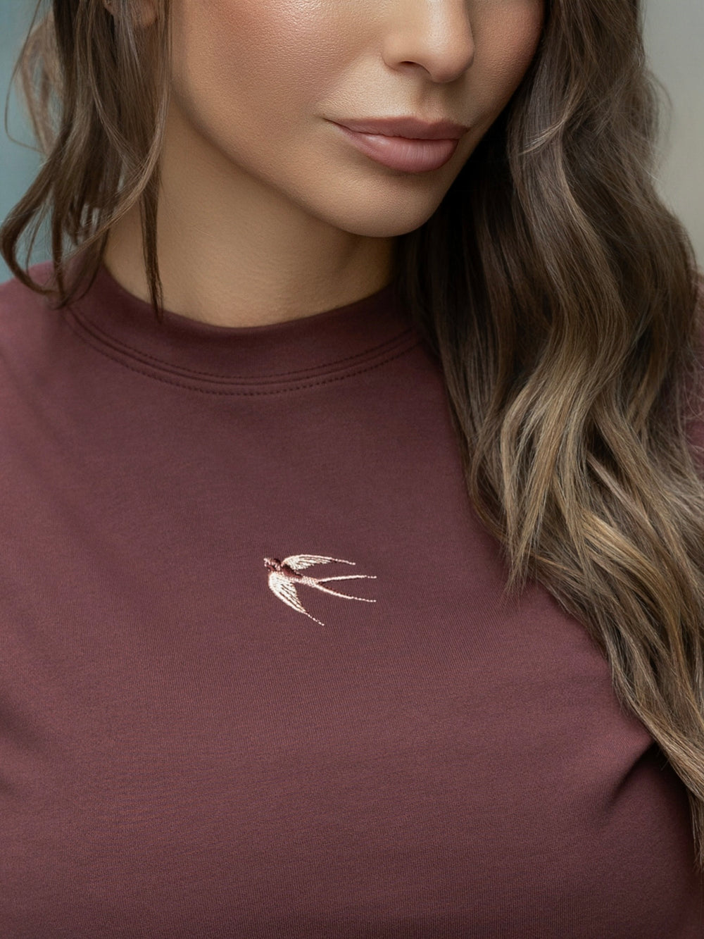 Close-up of a person wearing a maroon sweatshirt with a small embroidered design on the chest.