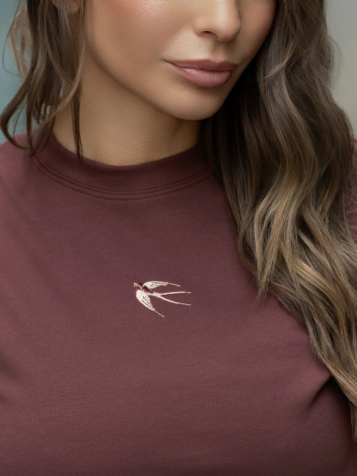 Close-up of a person wearing a maroon sweatshirt with a small embroidered design on the chest.